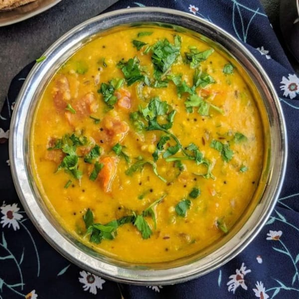 A silver bowl of yellow Indian dal, garnished with fresh green cilantro, on a dark floral napkin.
