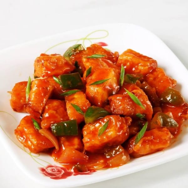 A white plate filled with vibrant orange chili paneer, green bell peppers, and onions.