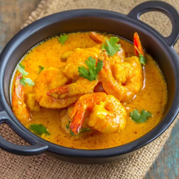 Indian shrimp curry in a black bowl, garnished with fresh cilantro and red chili.
