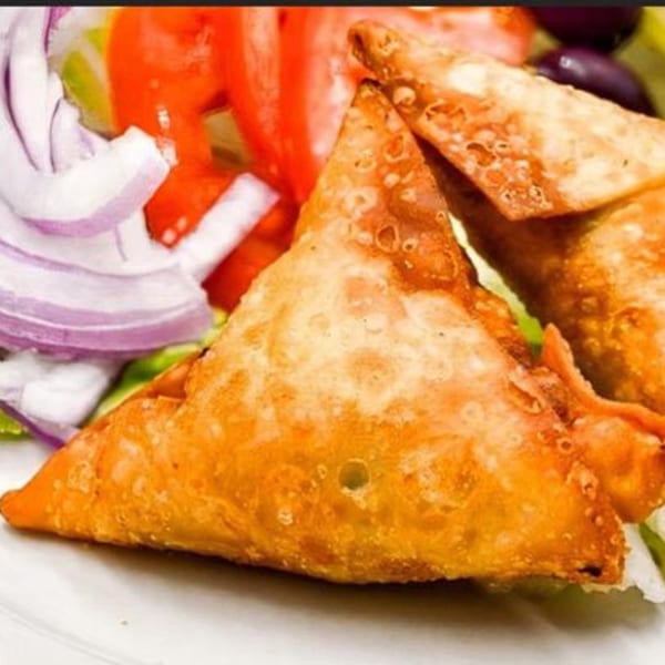 Golden-brown samosas on a white plate, garnished with fresh red tomatoes, purple onions, and green lettuce.