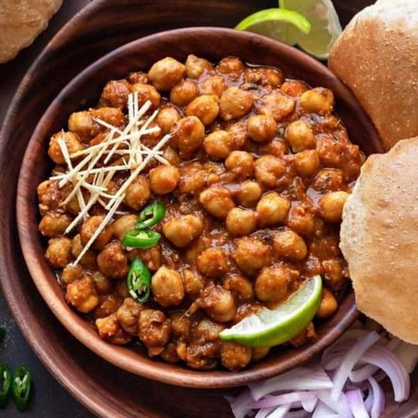 A bowl of chana masala with ginger, green chilies, lime, onions, and puri bread.
