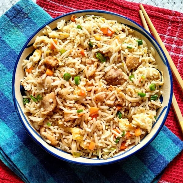Chicken fried rice with vegetables and egg in a blue and white bowl with chopsticks.