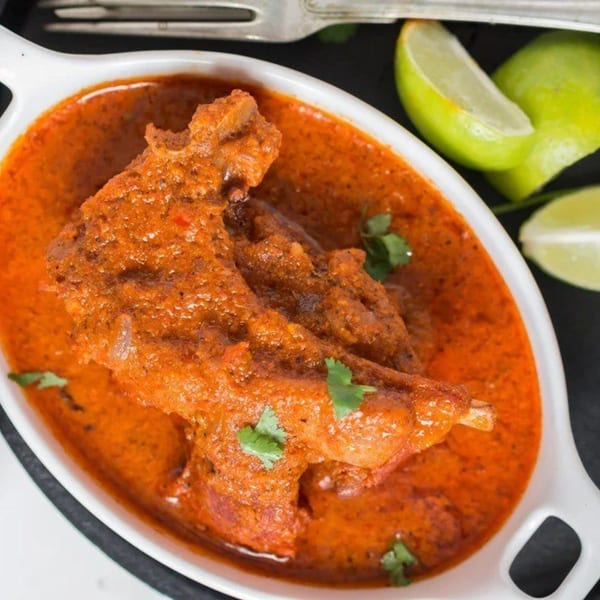 Indian chicken curry in a white dish, garnished with cilantro and lime wedges.
