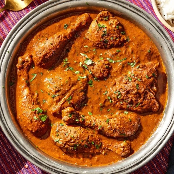 All India Authentic Cuisine's chicken curry, garnished with fresh herbs, in a silver serving dish.